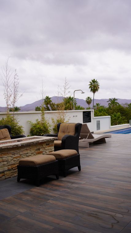 Un patio con sillas y otomanas junto a una piscina en un día nublado.