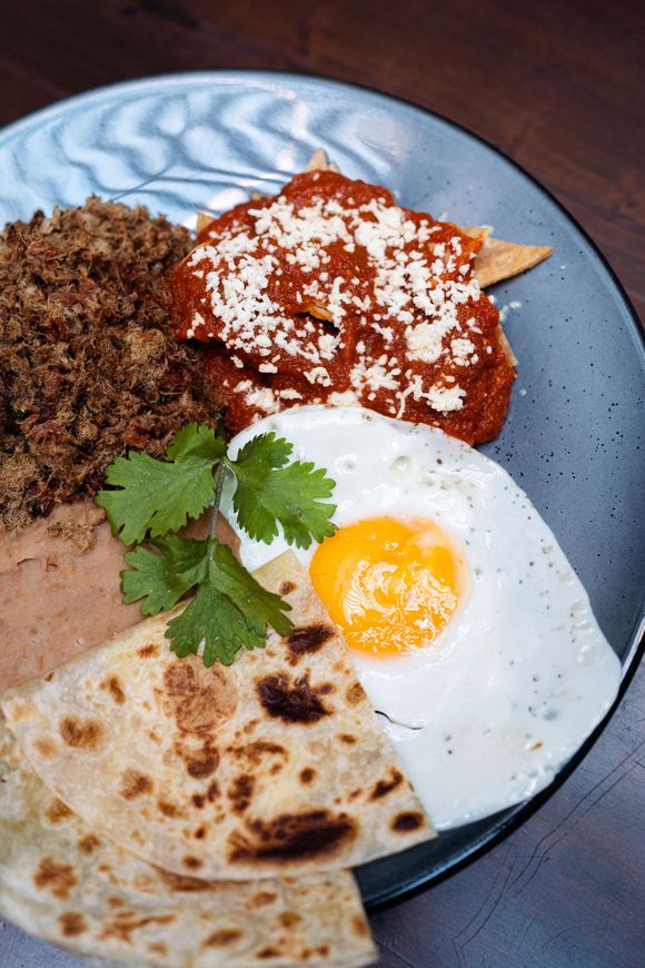 Un primer plano de un plato de comida con huevos, tortillas fritas y salsa sobre una mesa.