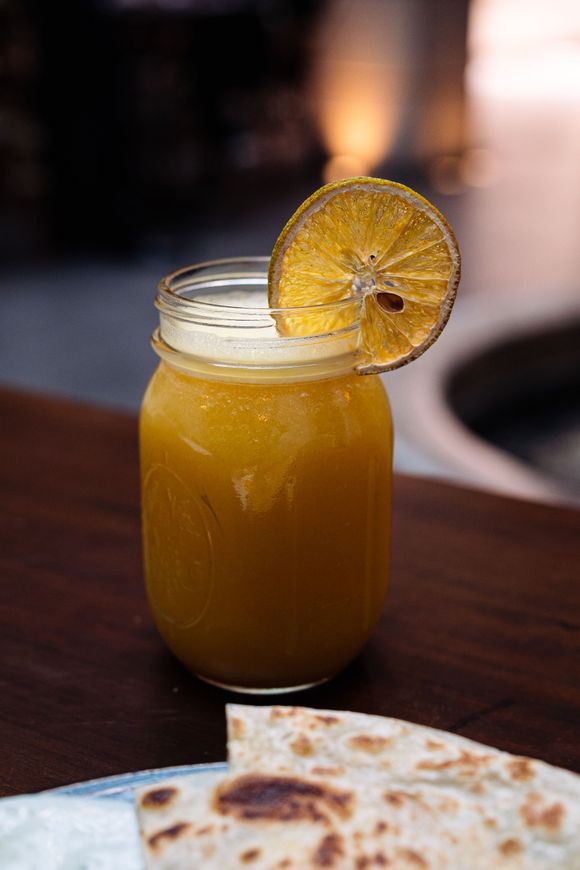 Un frasco de vidrio lleno de una bebida con una rodaja de naranja encima.