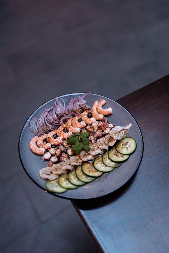 Un plato de comida con camarones, pulpo, pepinos y cebollas sobre una mesa.