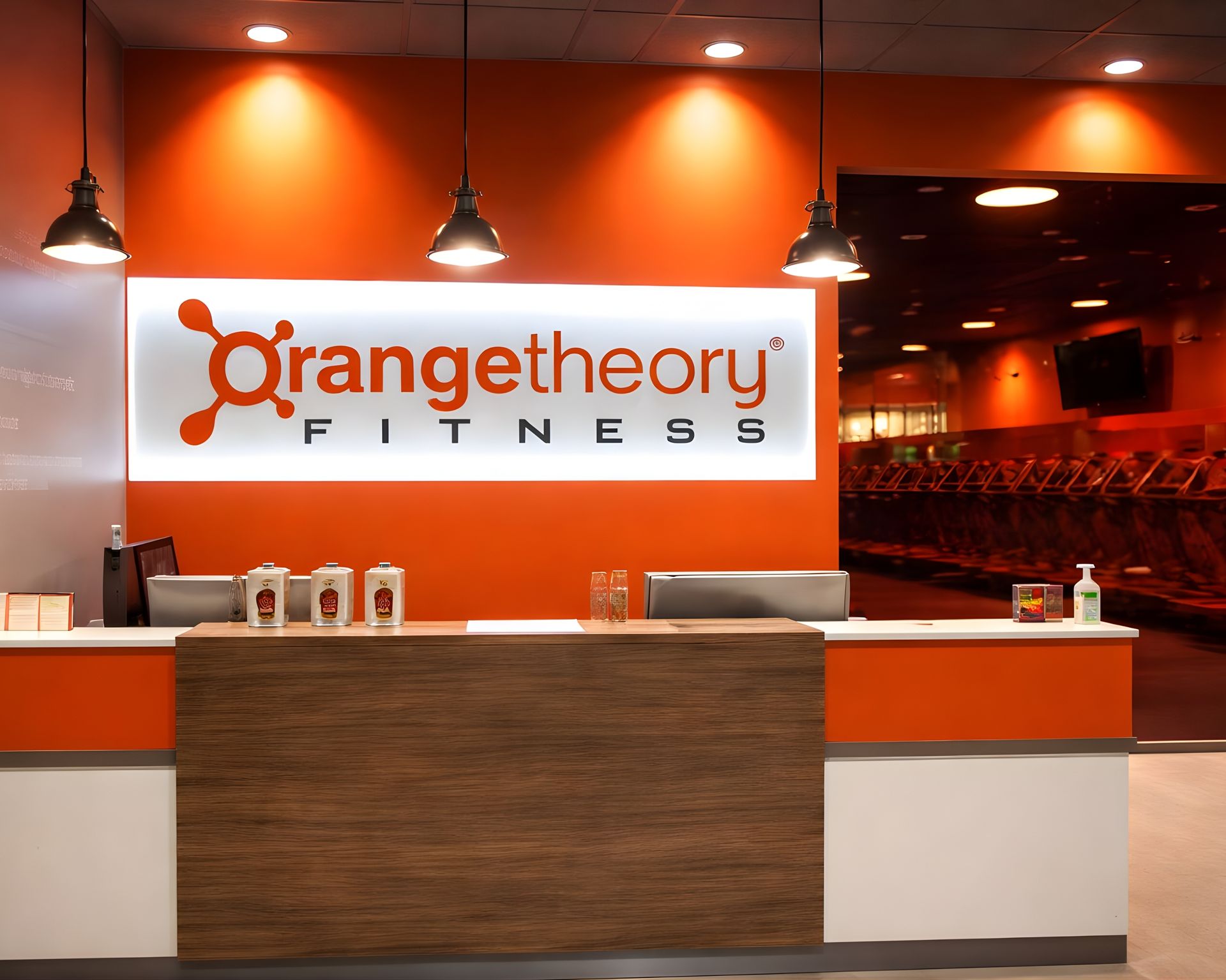 Orange Theory Fitness front desk with orange walls, pendant lights, and wood reception counter