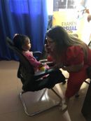 Mujer vestida de rojo se inclina hacia un niño sentado en una silla durante una visita a una clínica para un examen de la vista.