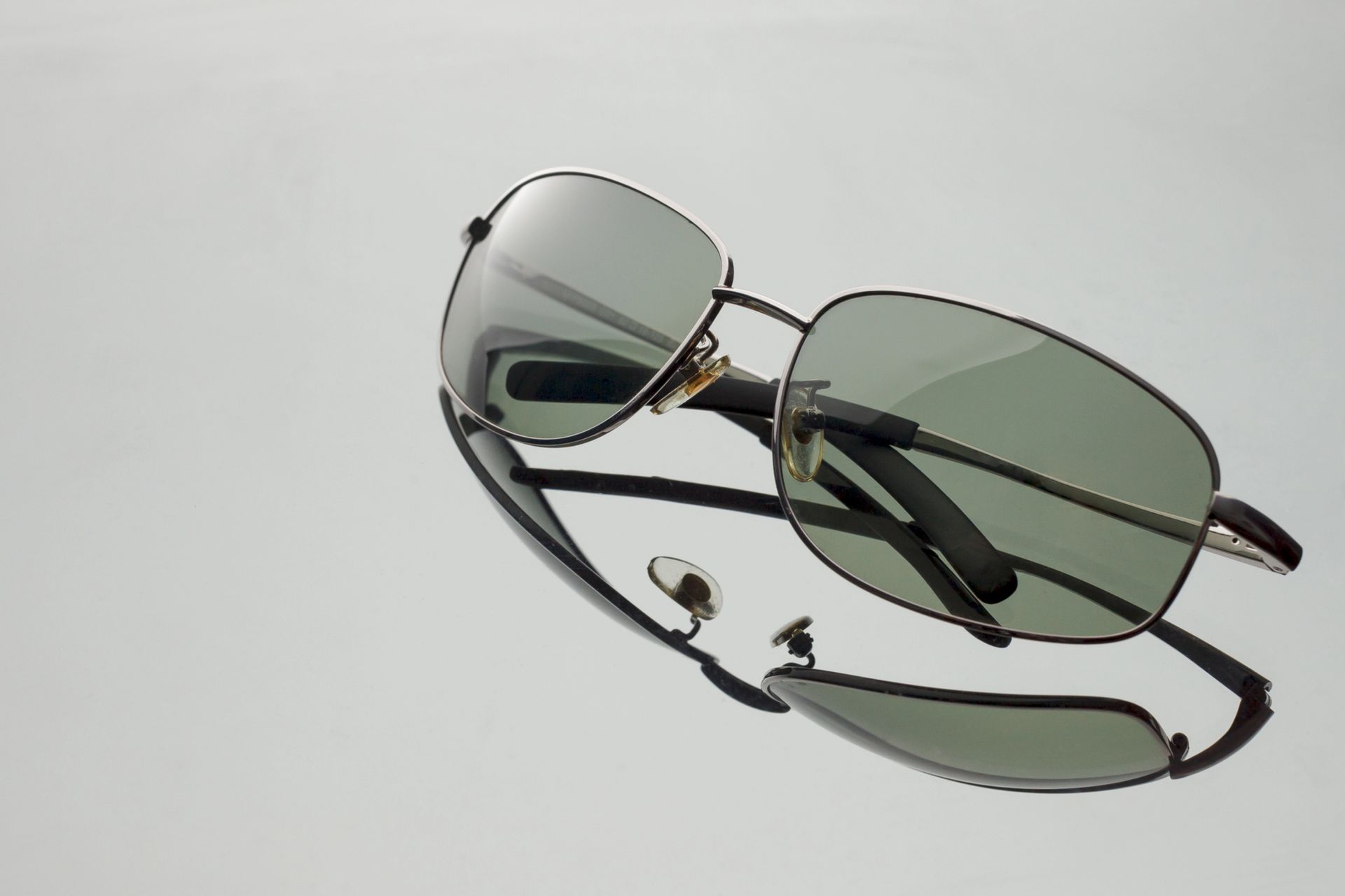 Gafas de sol con montura plateada y lentes tintadas de verde sobre fondo gris claro.