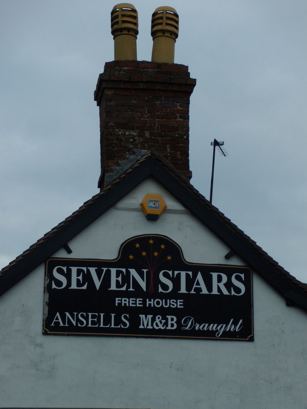Pub sign for Seven Stars free house, Ansells M&B Draught, on a white building with a brick chimney.