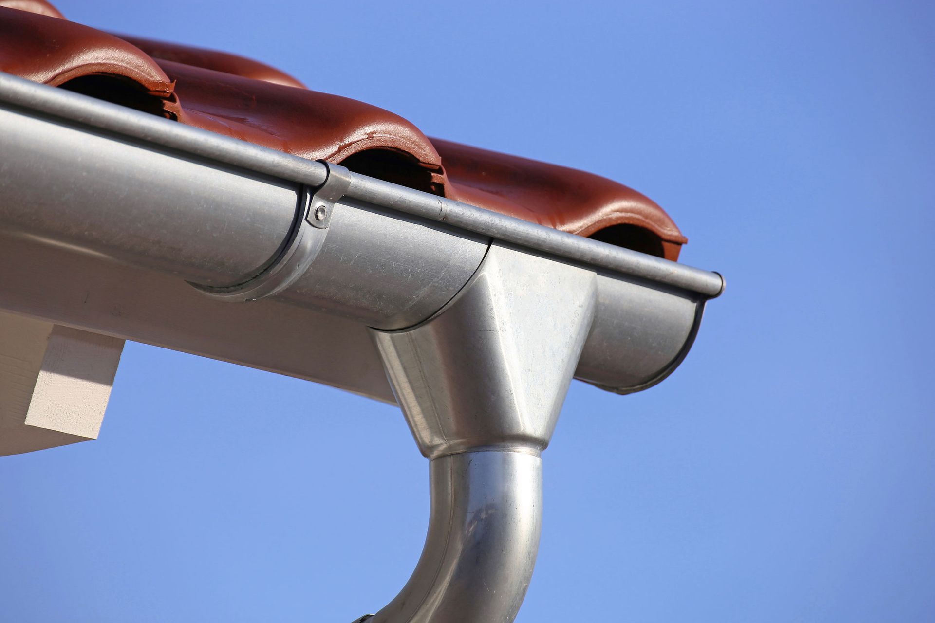 A close up of a steel gutter on a roof with a blue sky in the background.