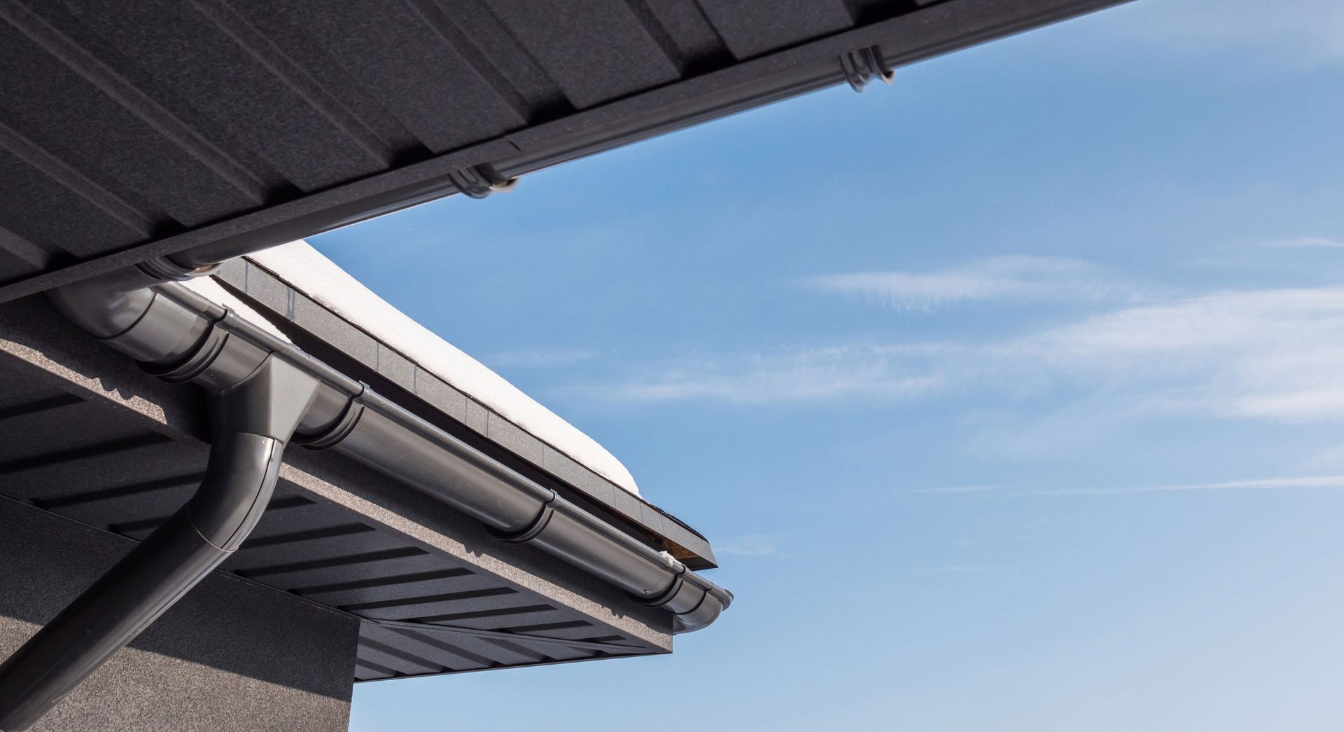 A close up of a gutter on a roof with a blue sky in the background.