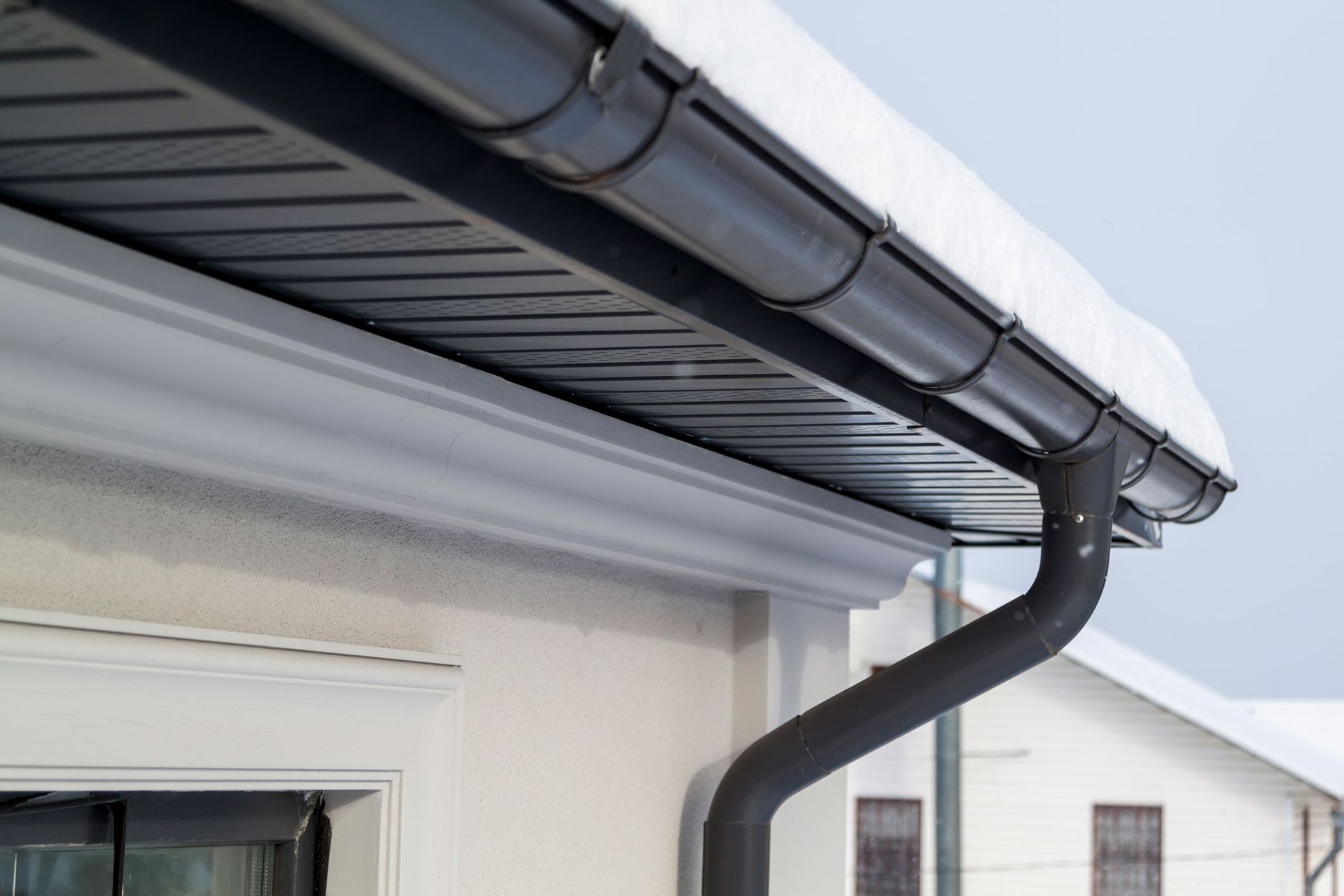 A gutter on the side of a house with snow on it.