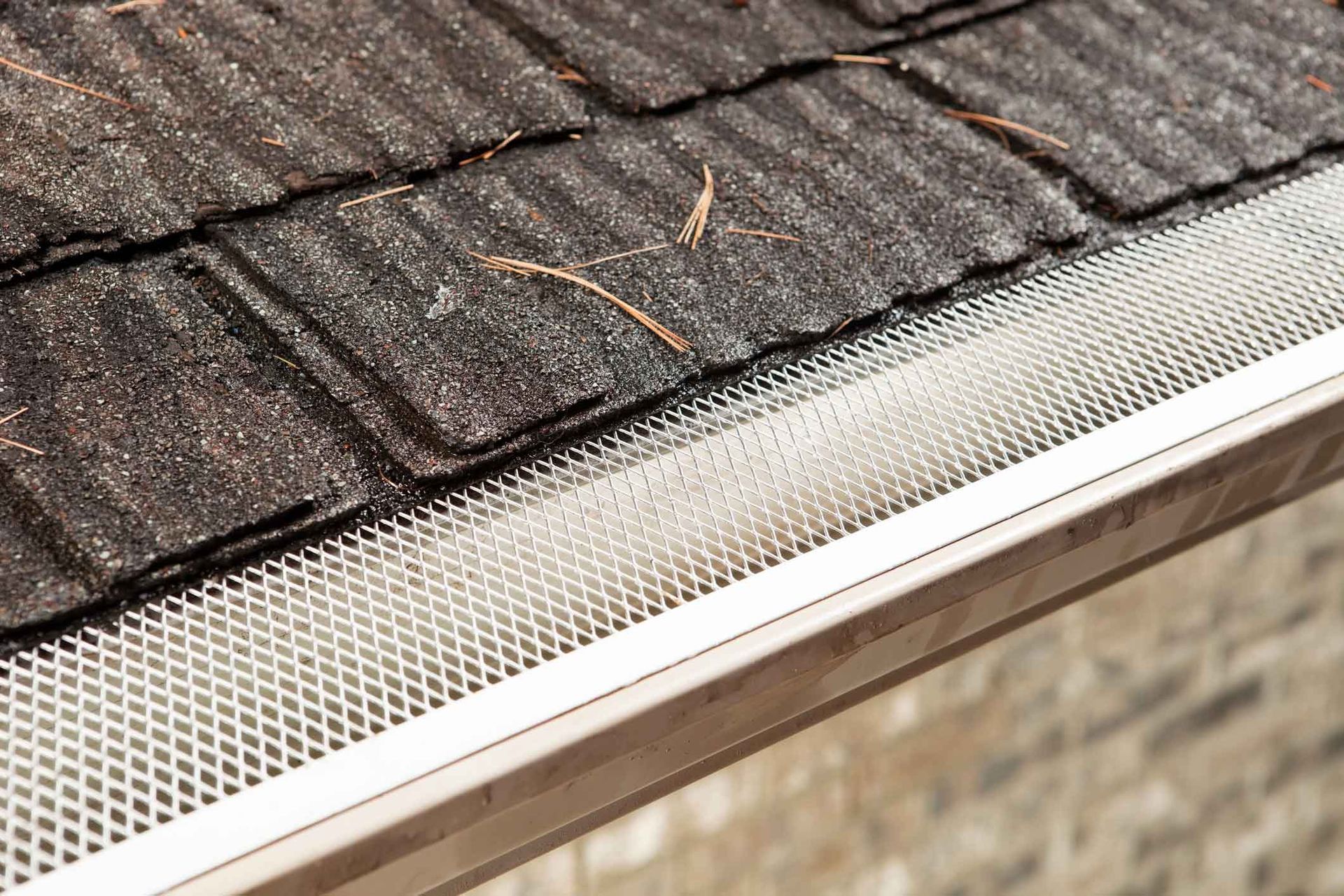 A close up of a gutter on a roof with shingles.