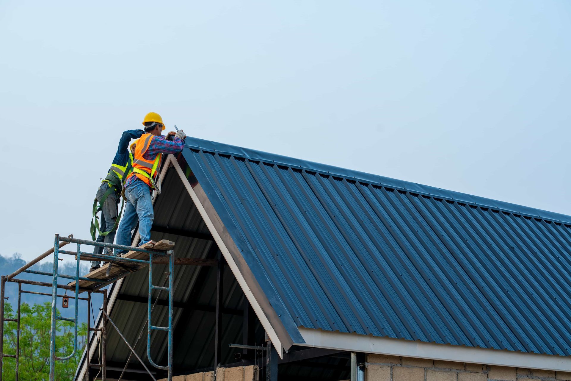 Workers installing a blue metal roof on a house from a scaffold