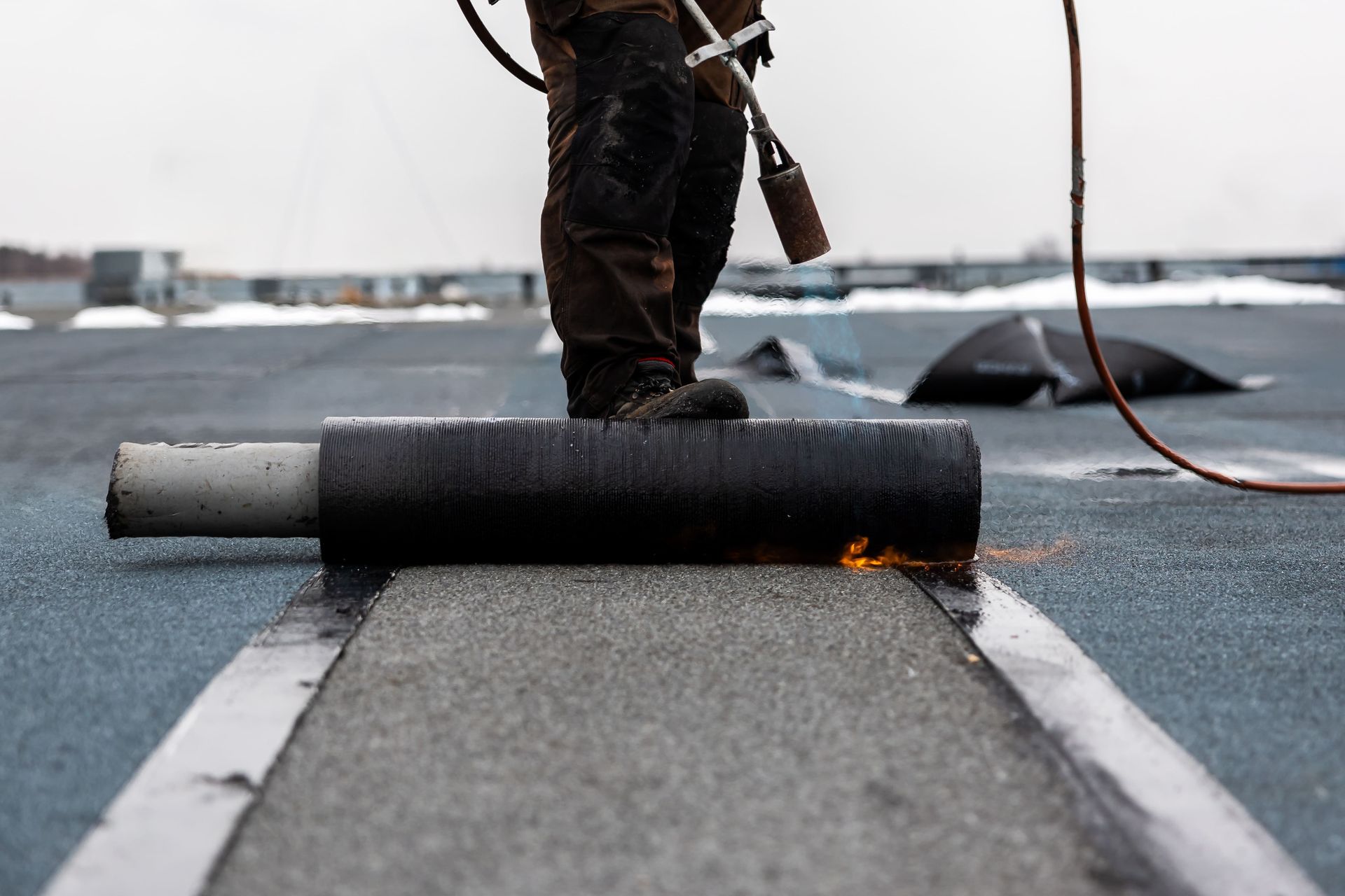 Worker using a torch to seal a rolled roofing membrane on a flat roof