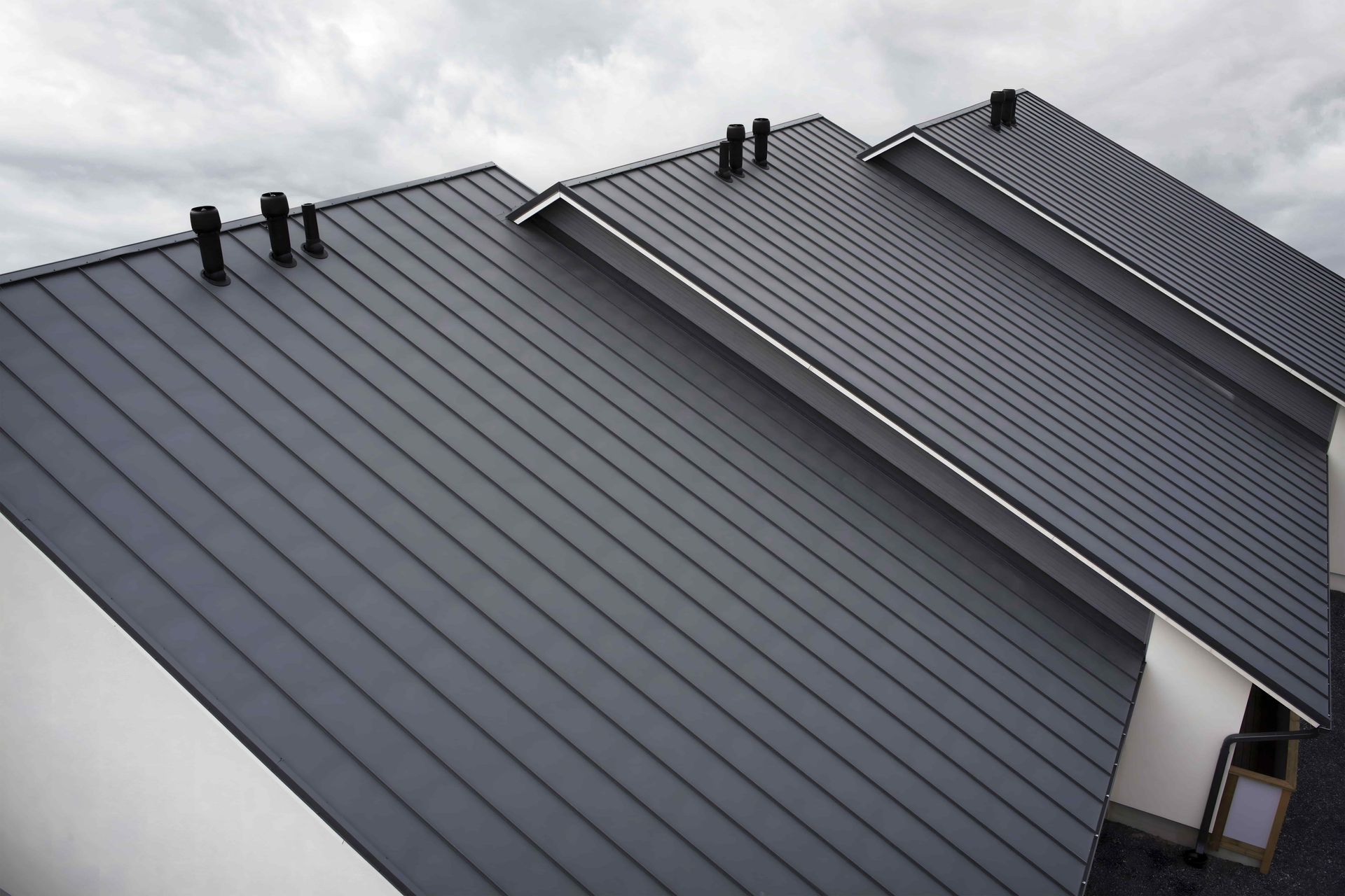 Three dark gray metal roofs with standing seams and vents, viewed from above