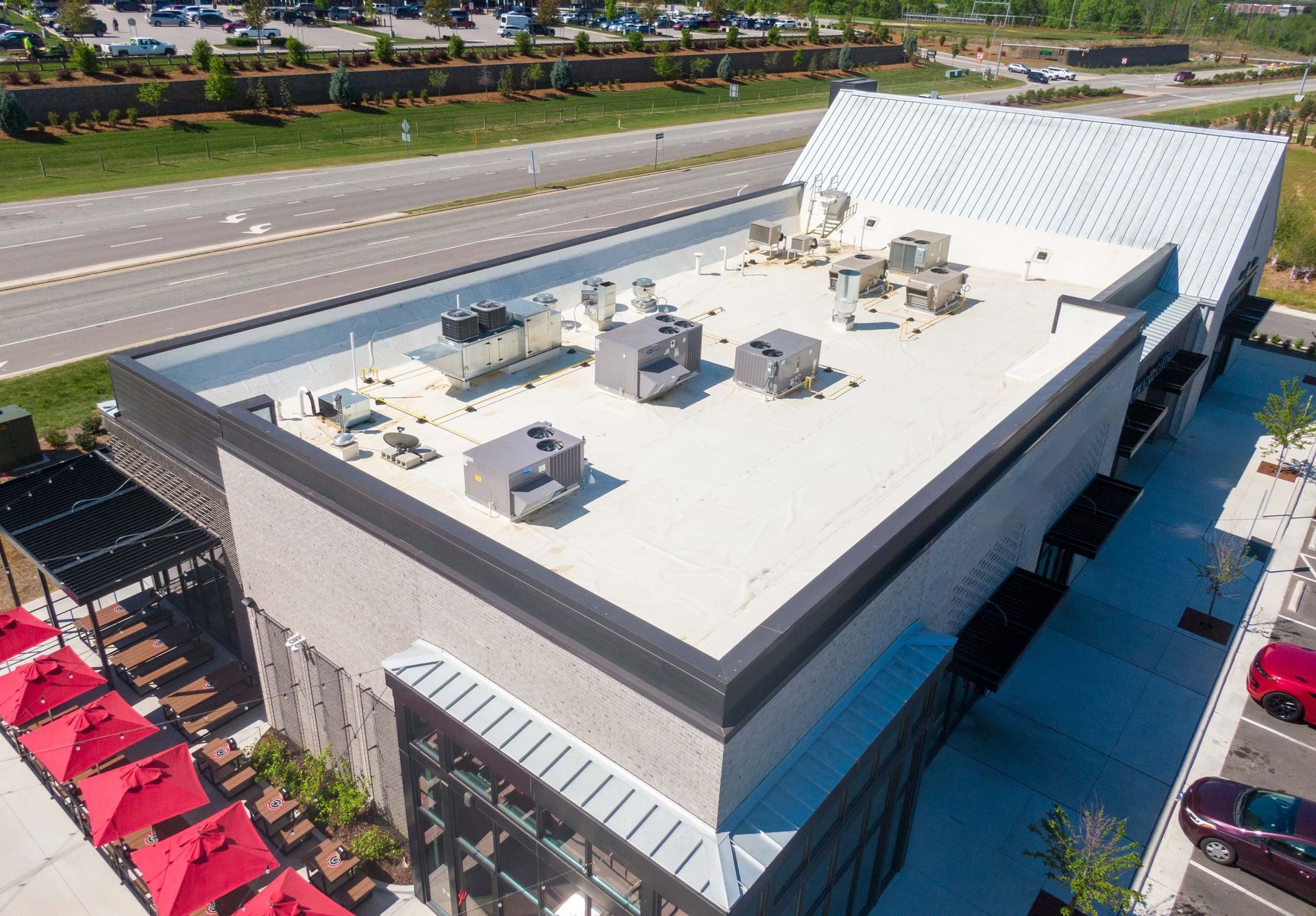 Aerial view of a white commercial building with rooftop units beside a highway