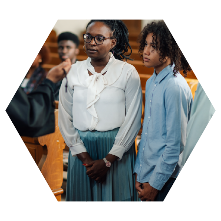 Adult and youth standing together inside a church, listening attentively during a service or community gathering