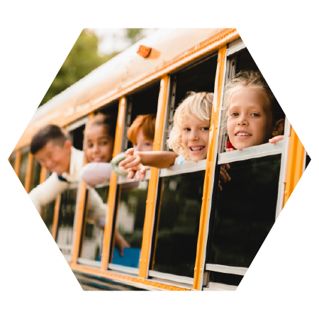 Smiling kids leaning out of a yellow school bus window, representing happy students and community involvement