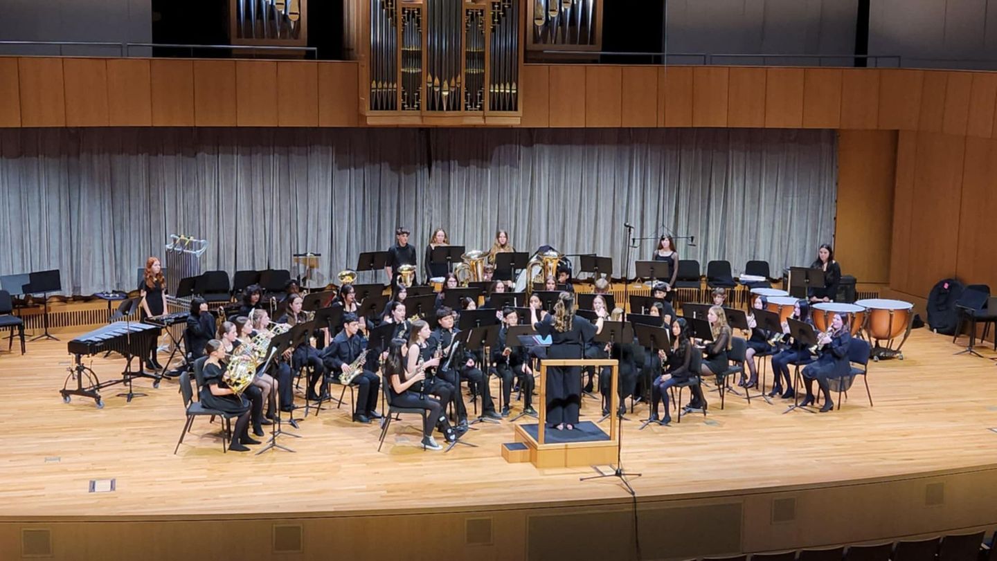School concert band performing on stage with student musicians and conductor.