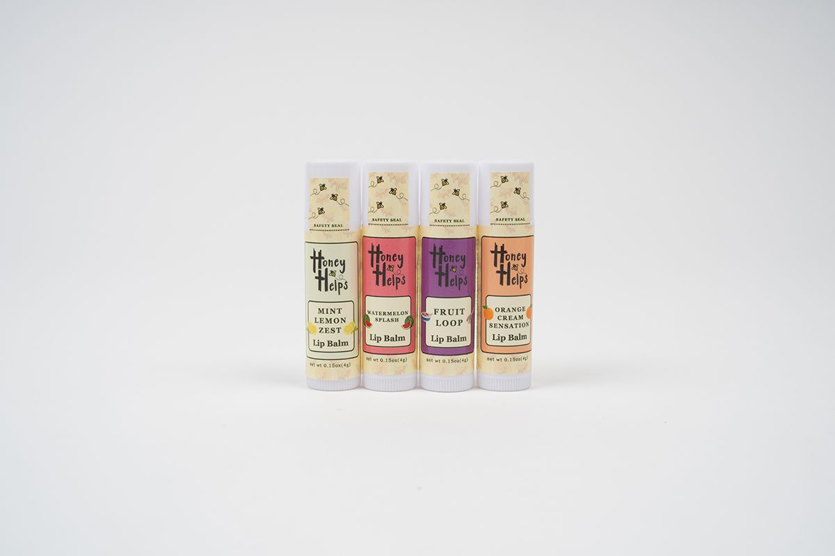 Four Honey Helps lip balm tubes in assorted flavors displayed upright on a clean white background