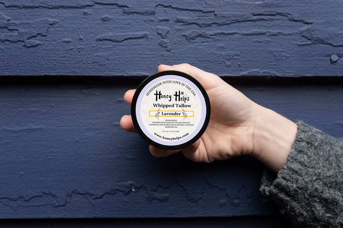 Hand holding Honey Helps lavender whipped tallow balm against a blue textured wall