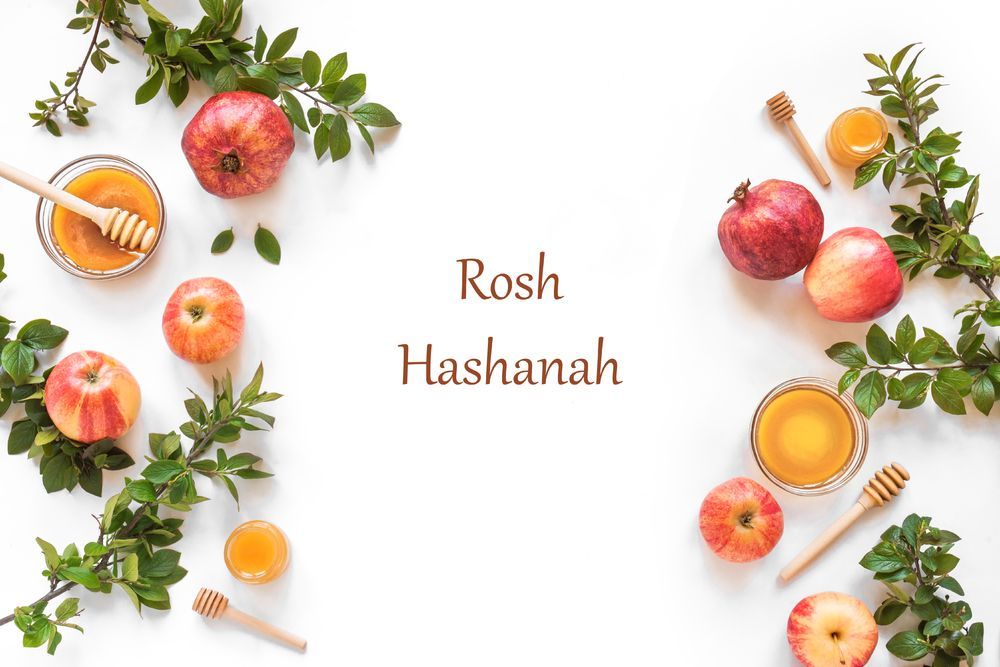 Apples, pomegranates, honey, and greenery arranged on white background, with