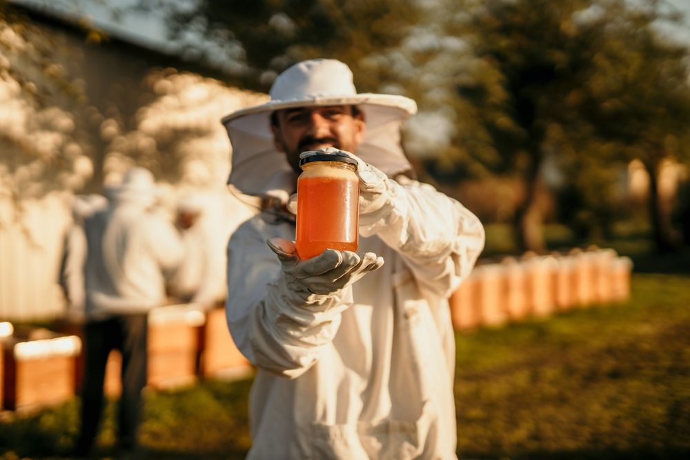 A beekeeper is holding a jar of honey in his hand.