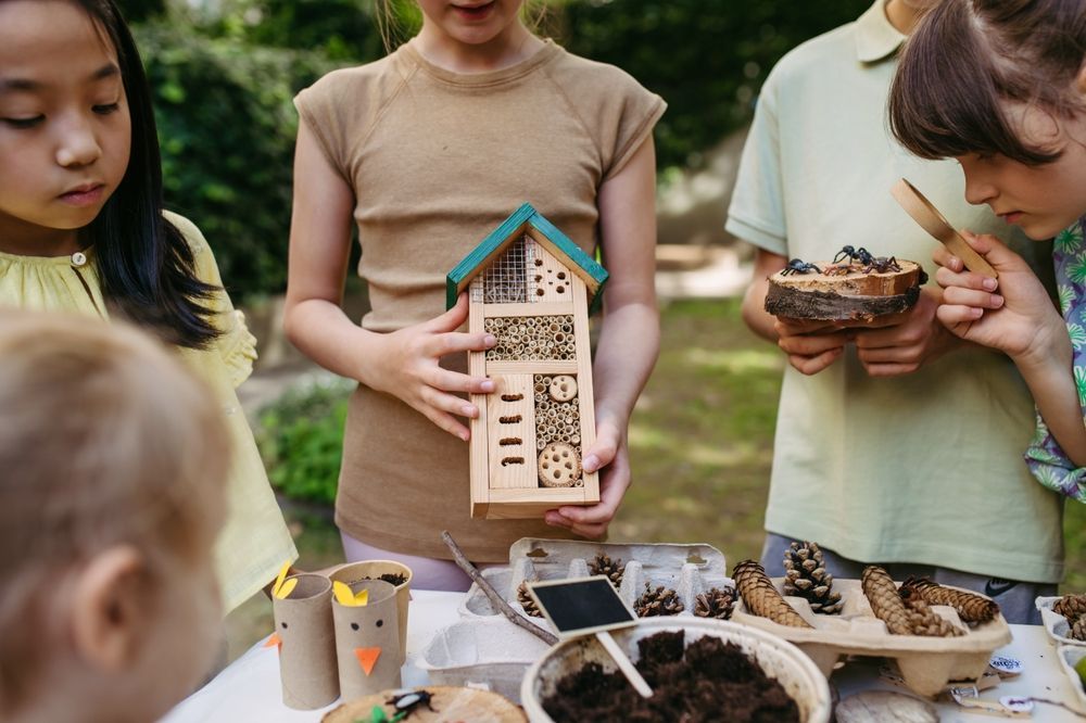 A group of children are standing around a table holding a bug house.