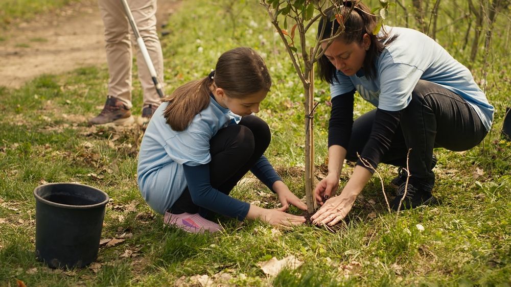 Mother and daughter planting a tree together during a community fundraising event outdoors.