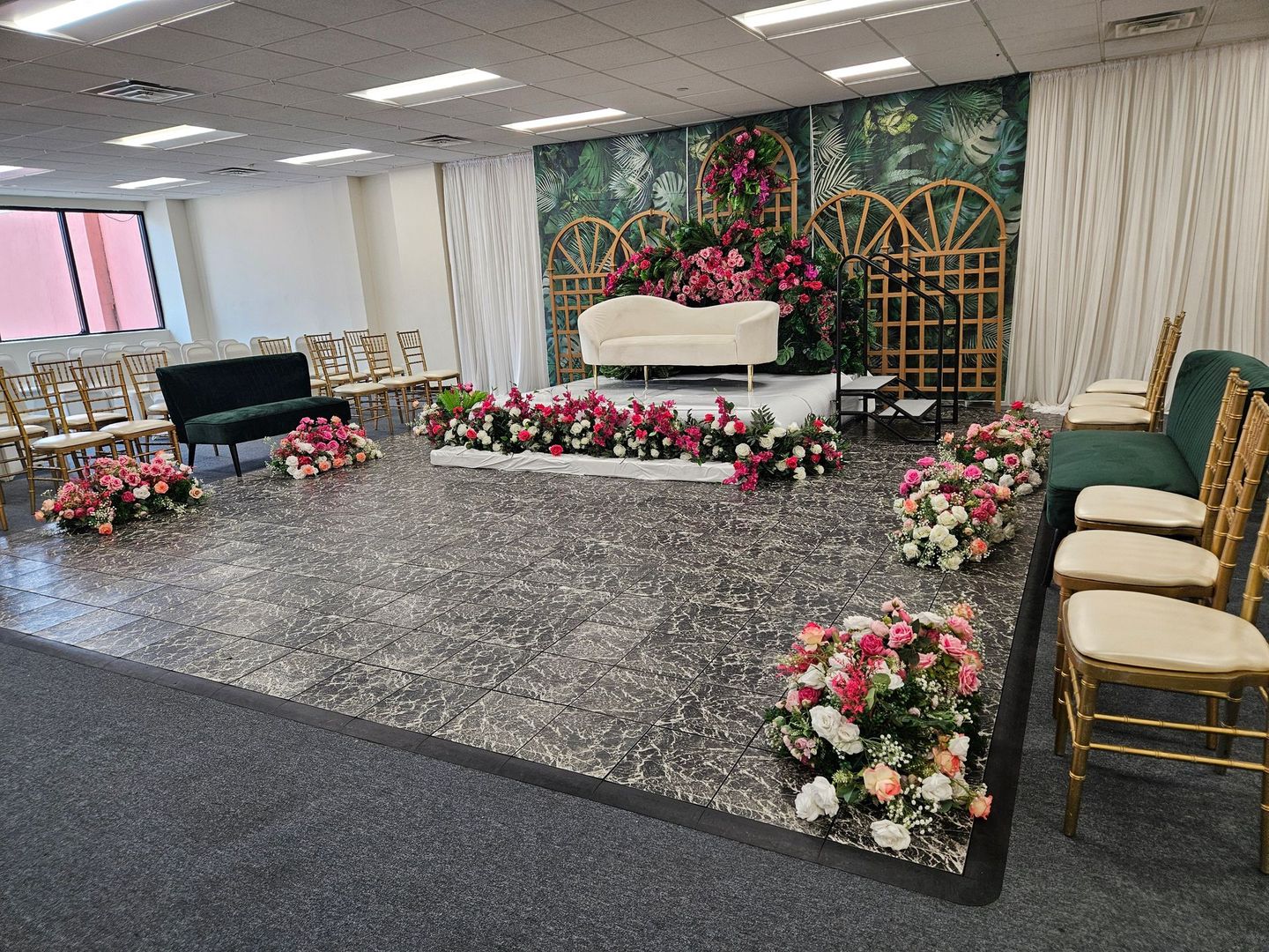 Floral-decorated stage with white chairs, pink flowers, and gold lattice backdrop in a banquet hall