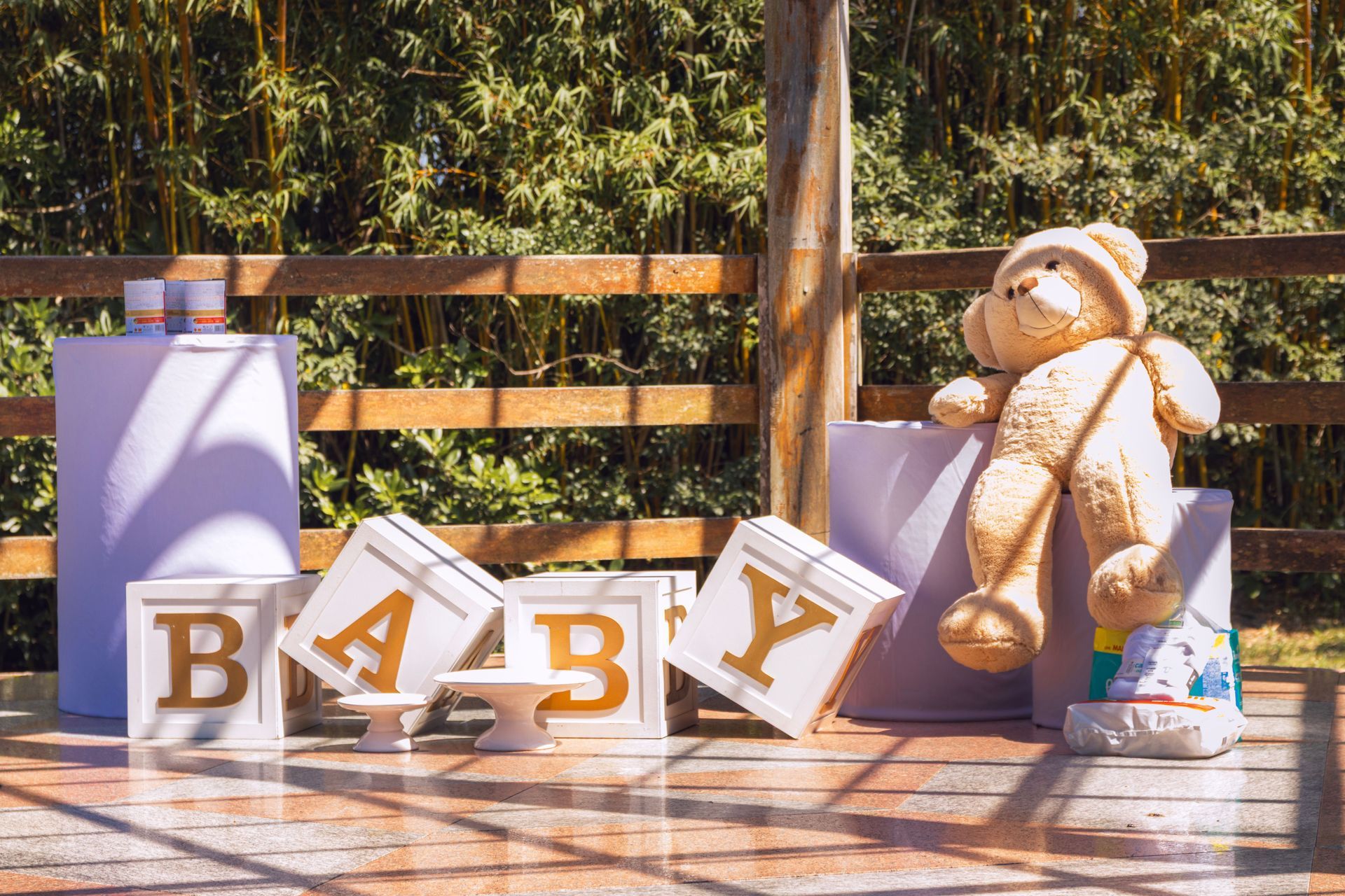 BABY letters and teddy bear on a bench outdoors, with a lavender gift box nearby