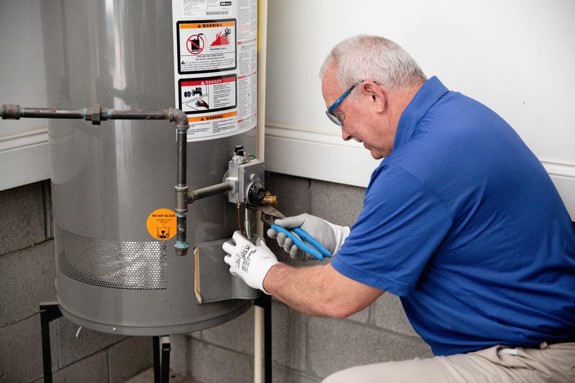 Technician in blue shirt inspecting a water heater with tools in a utility room