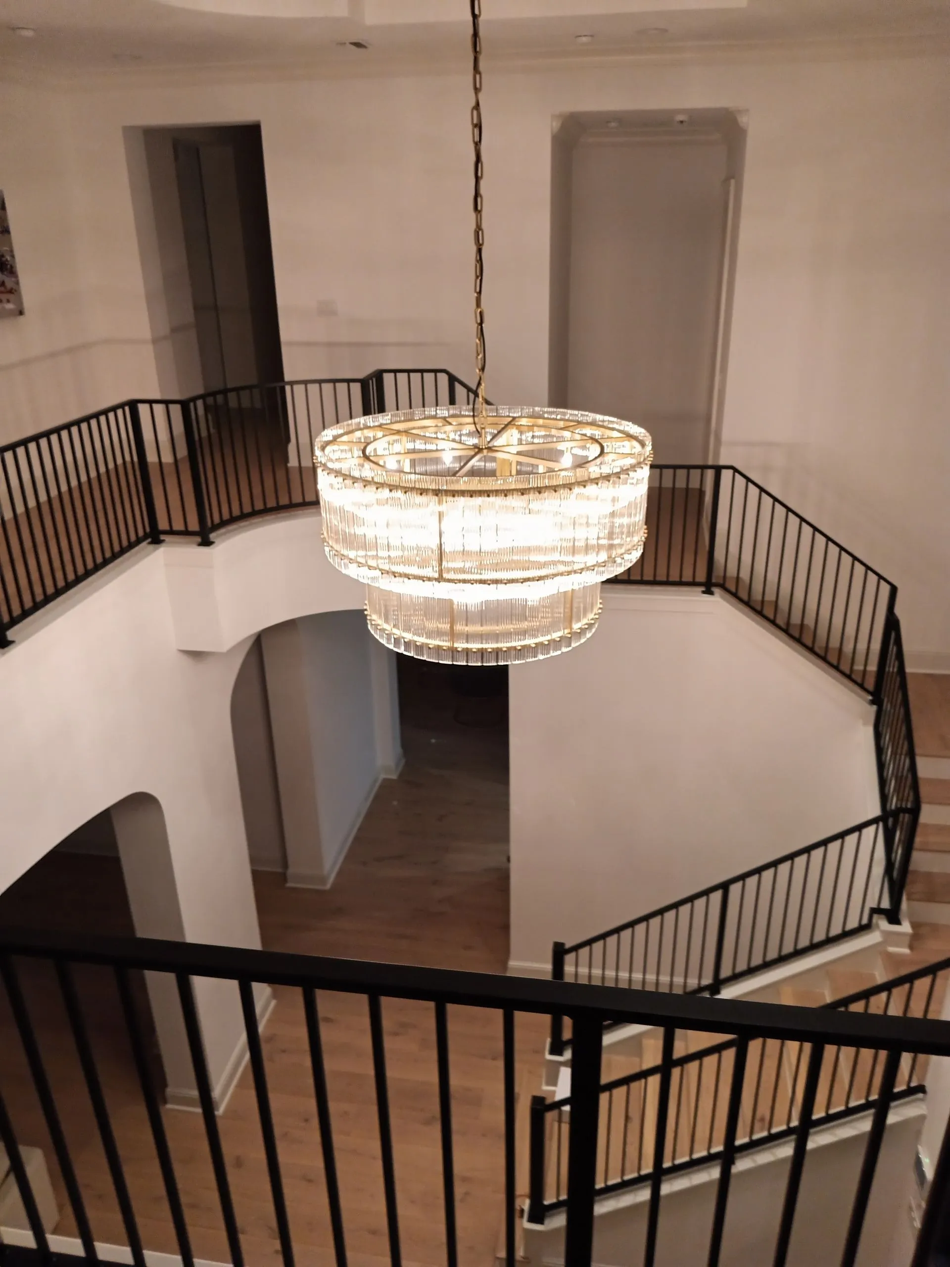 Elegant chandelier hanging in a bright two-story foyer with black railings and wooden floors