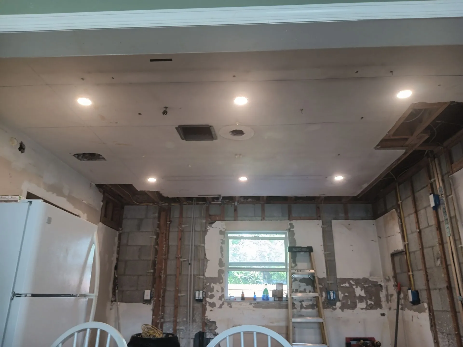 Partially renovated kitchen with exposed walls, ceiling lights, and a window over the sink