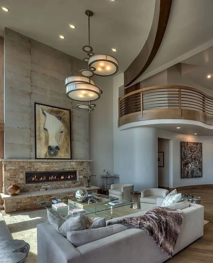 Spacious modern living room with curved balcony, stone fireplace, and neutral sectional seating