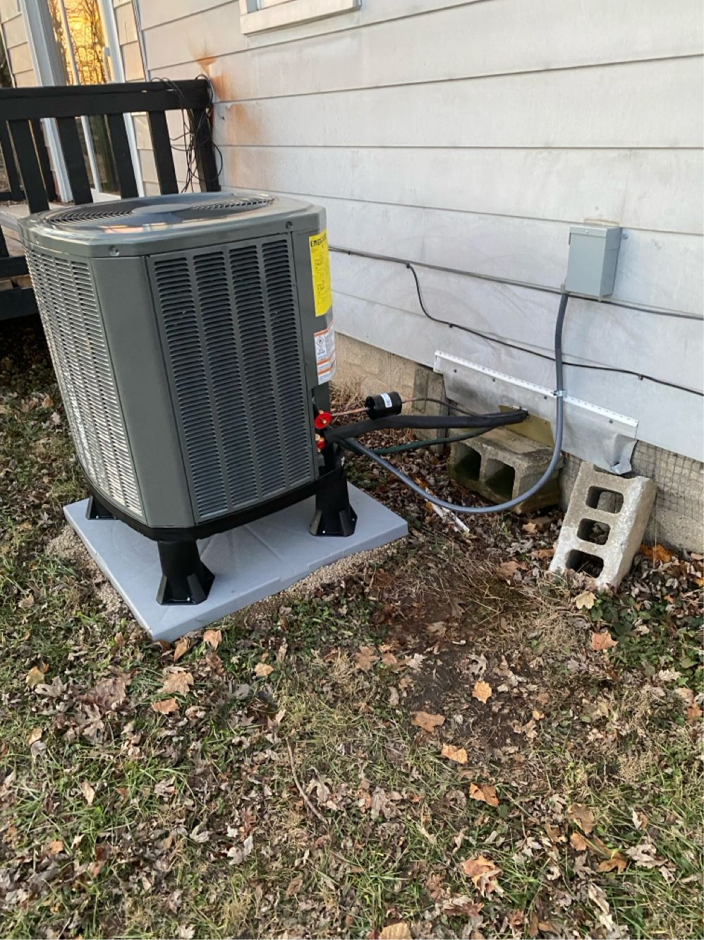 An air conditioner is sitting on top of a concrete platform next to a house.
