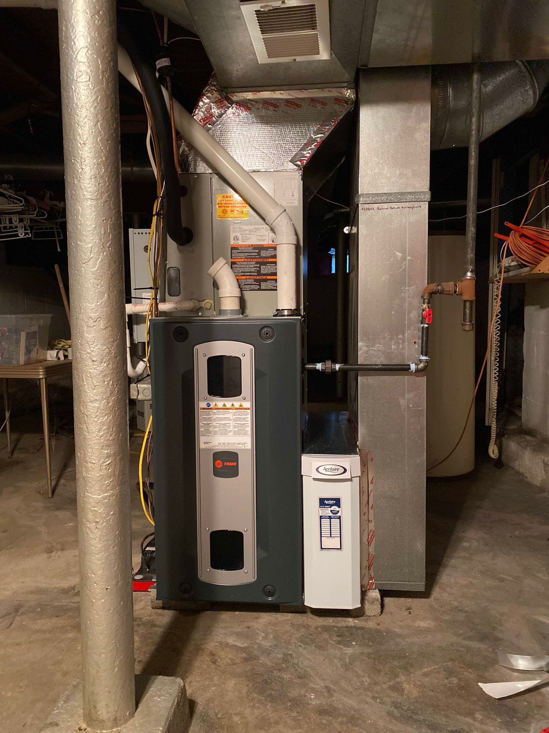 A gas heater is sitting in a basement next to a water heater.