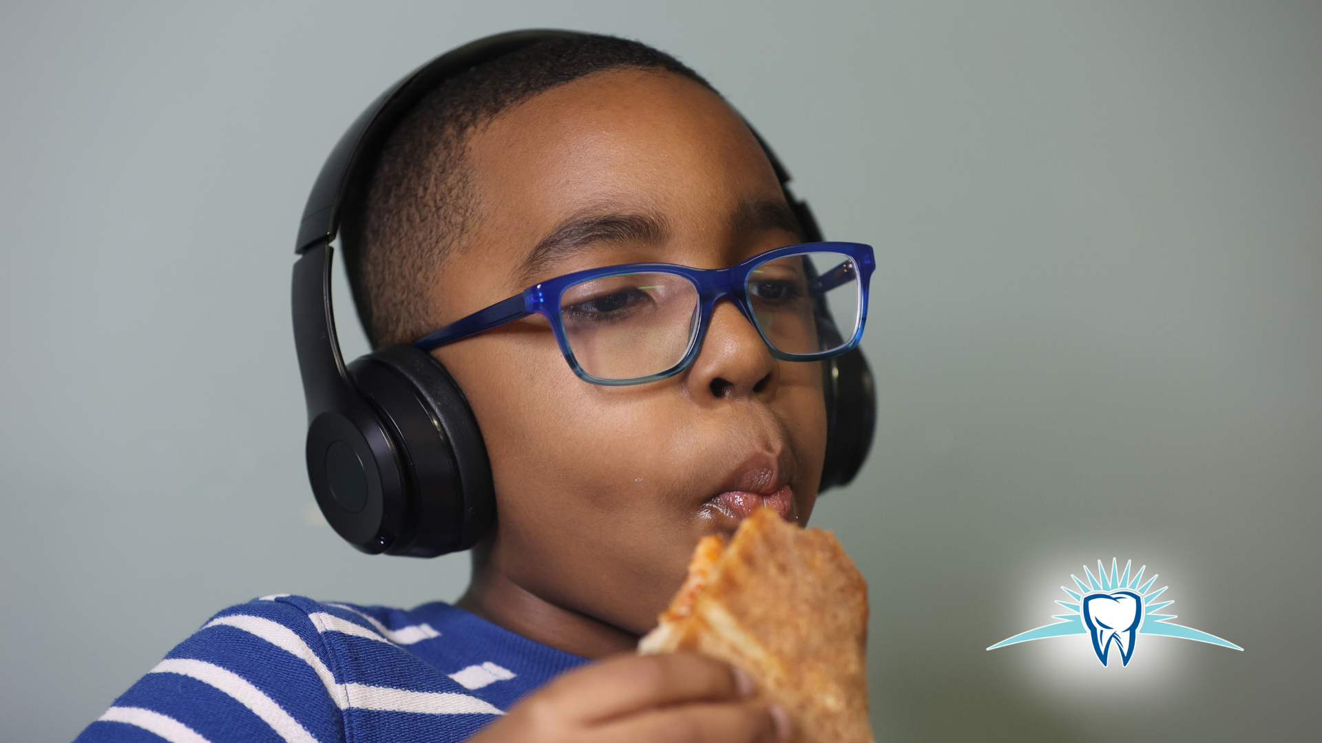 Boy wearing headphones and glasses, eating pizza.