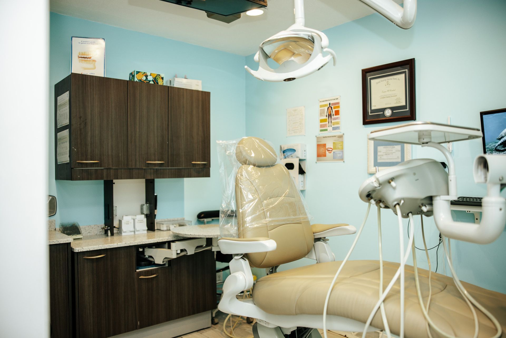 Dental office interior with beige chair, equipment, and cabinets, light blue walls.