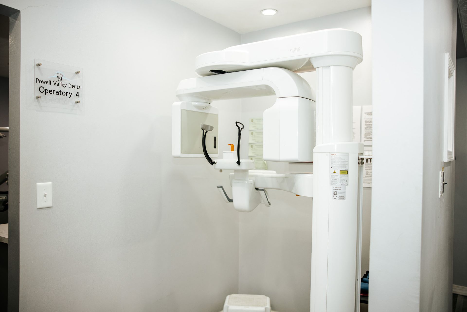 Dental X-ray machine in a bright white examination room; the device is large and complex.
