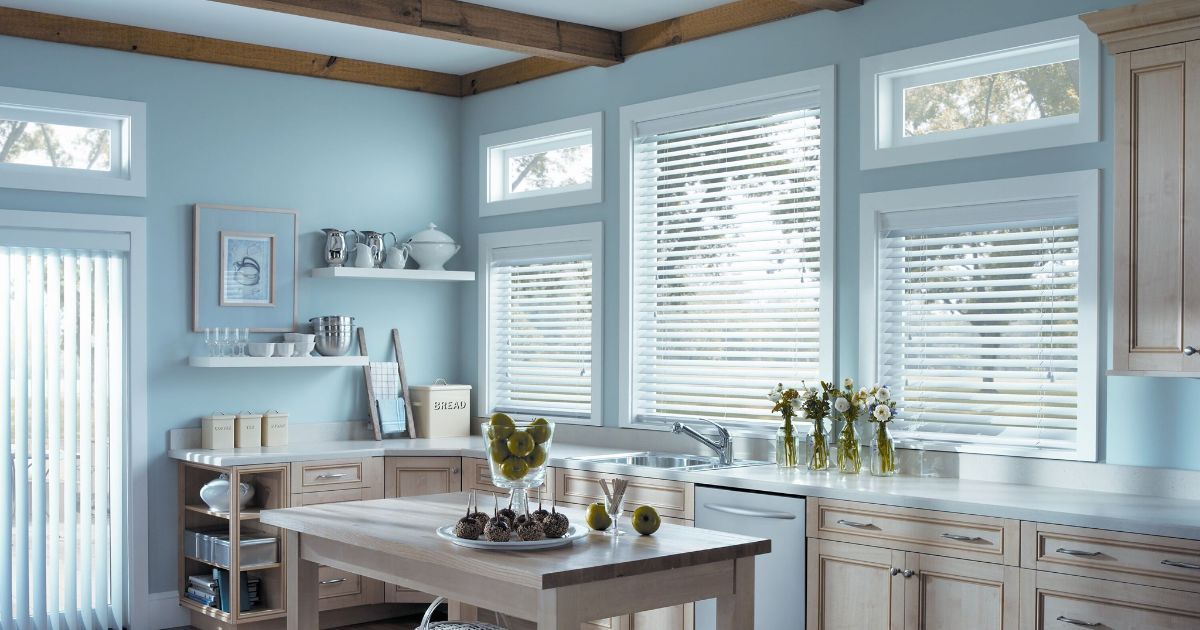 A kitchen with blue walls , white cabinets , and white blinds.