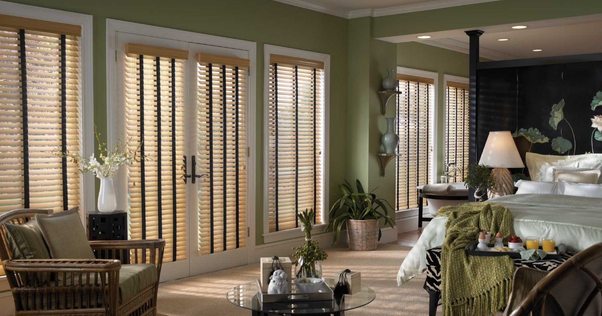 A faux wood blinds bedroom with a bed , chair , table and sliding glass doors.
