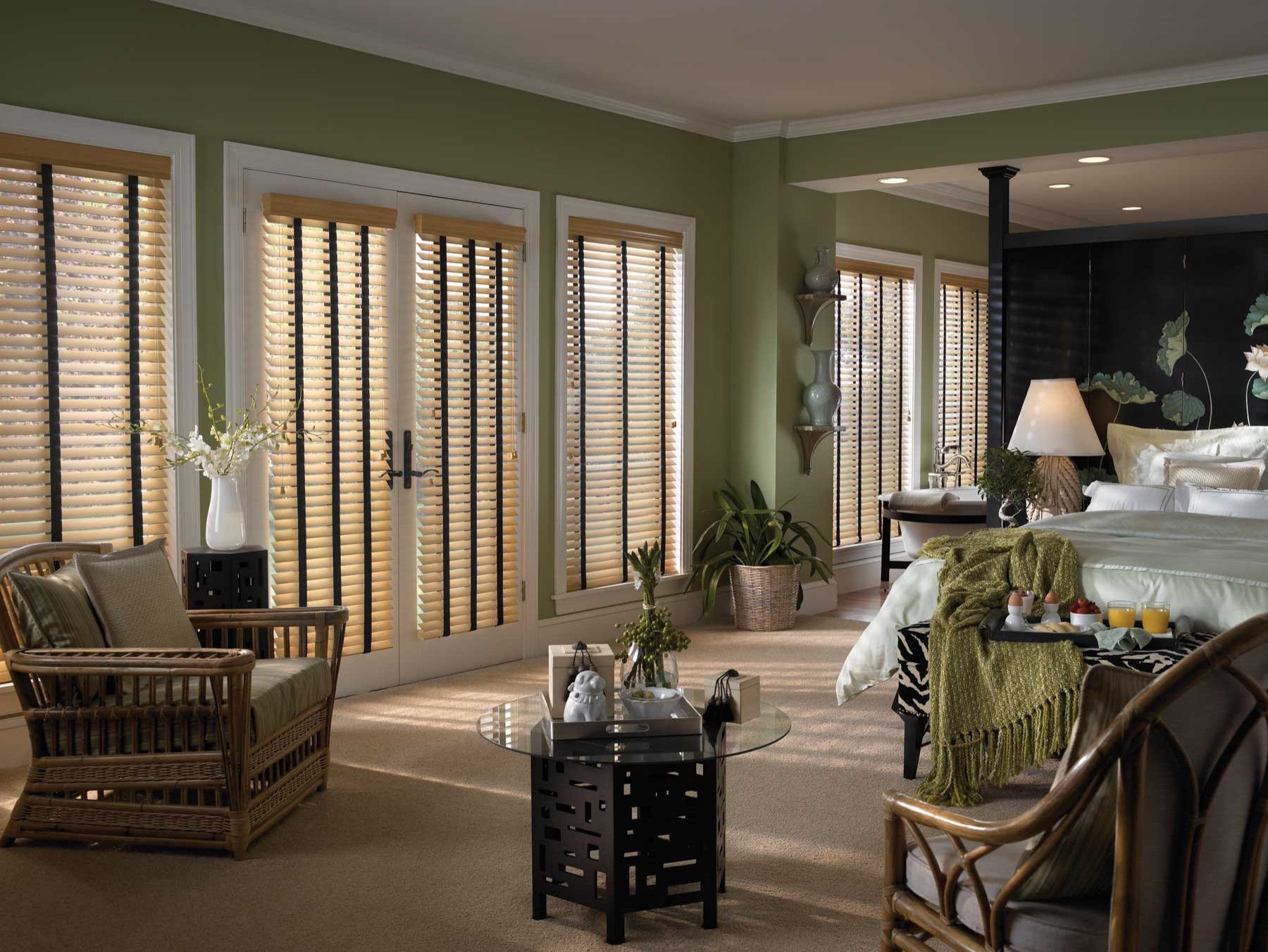 A living room with a window blinds, bed , chairs , coffee table and sliding glass doors.
