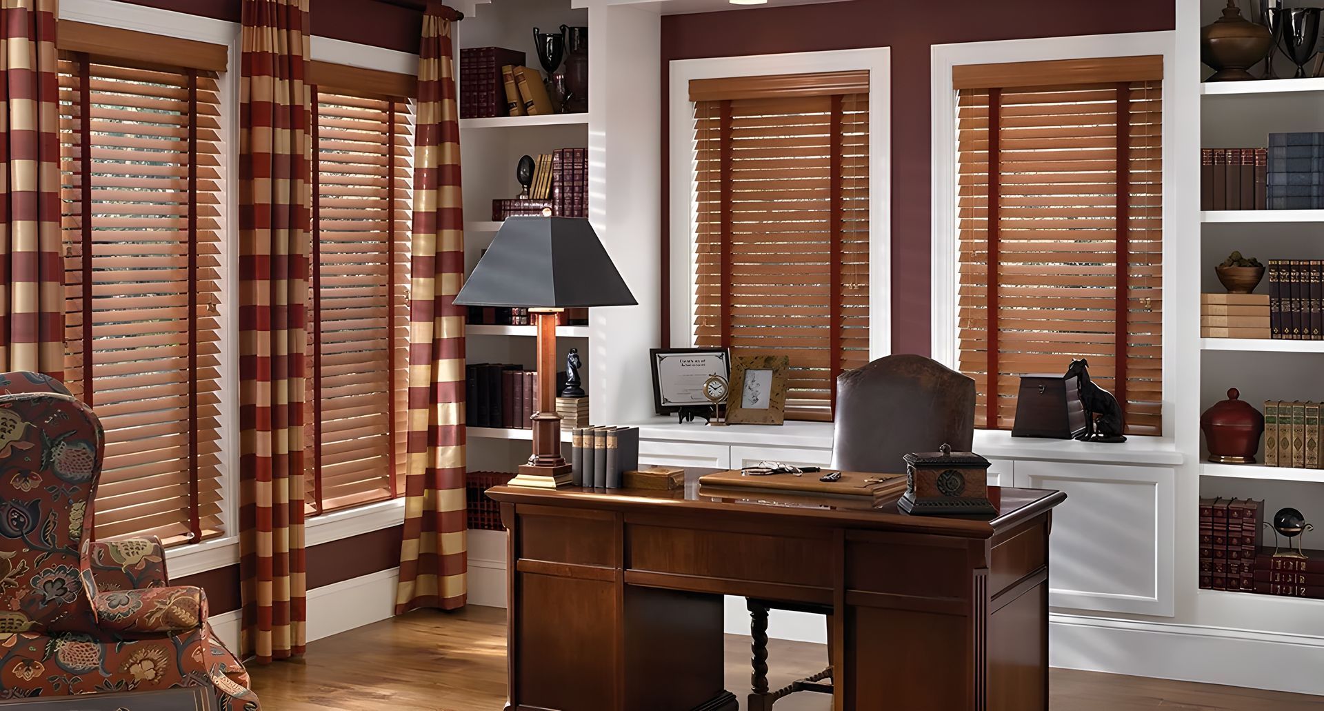A home office with wood blinds, wooden desk and a lamp