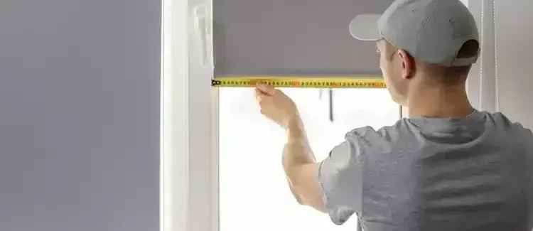 A man is measuring a window with a tape measure.