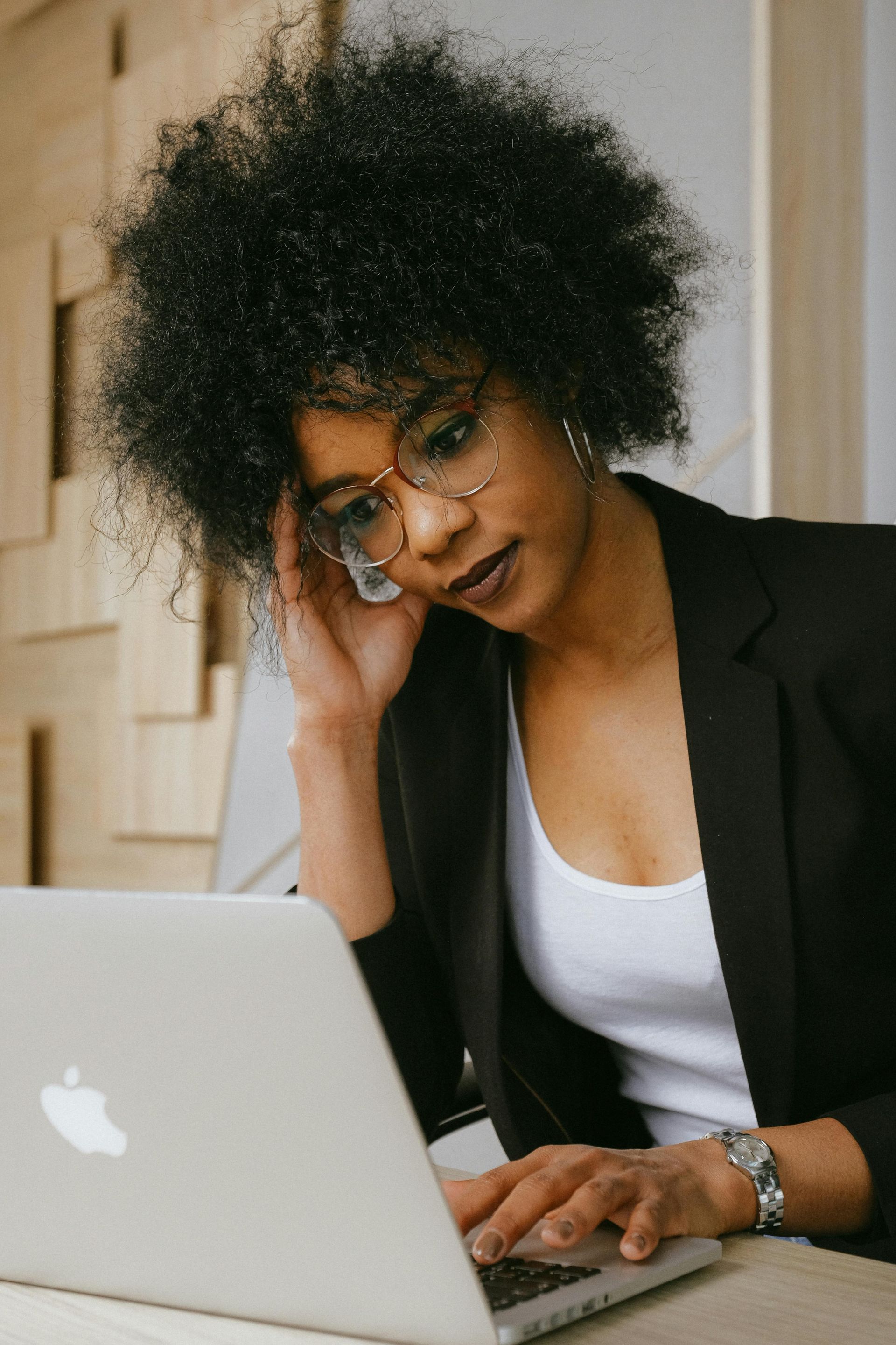 A woman is sitting at a table with her hands on her head in front of a laptop computer.
