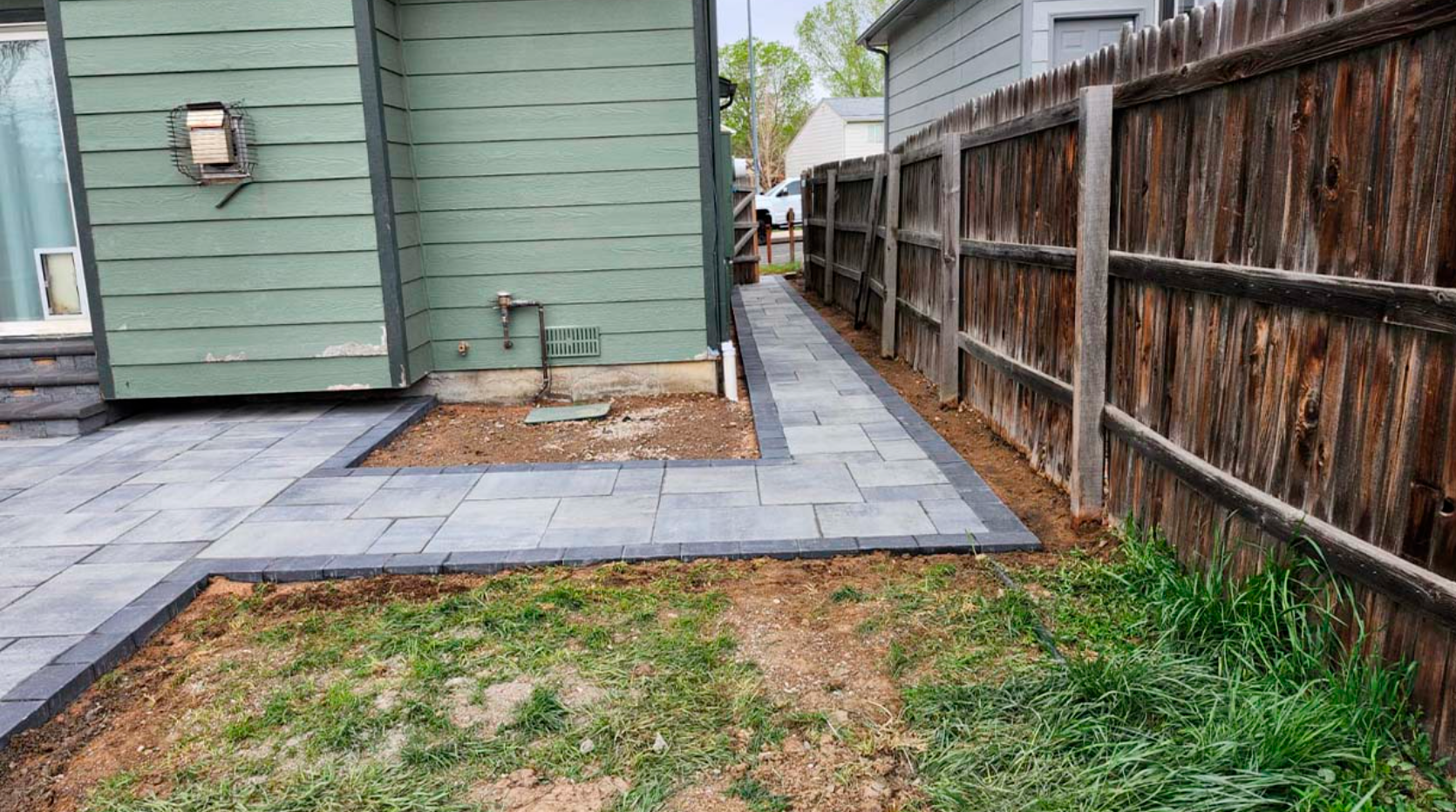 A sidewalk leading to a house next to a wooden fence.