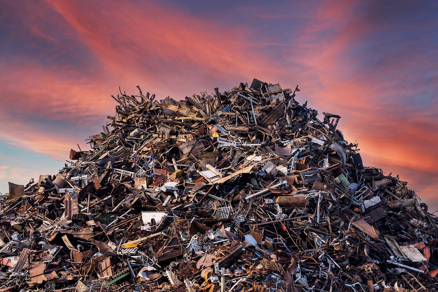 Large pile of scrap metal and debris under a colorful sunset sky.