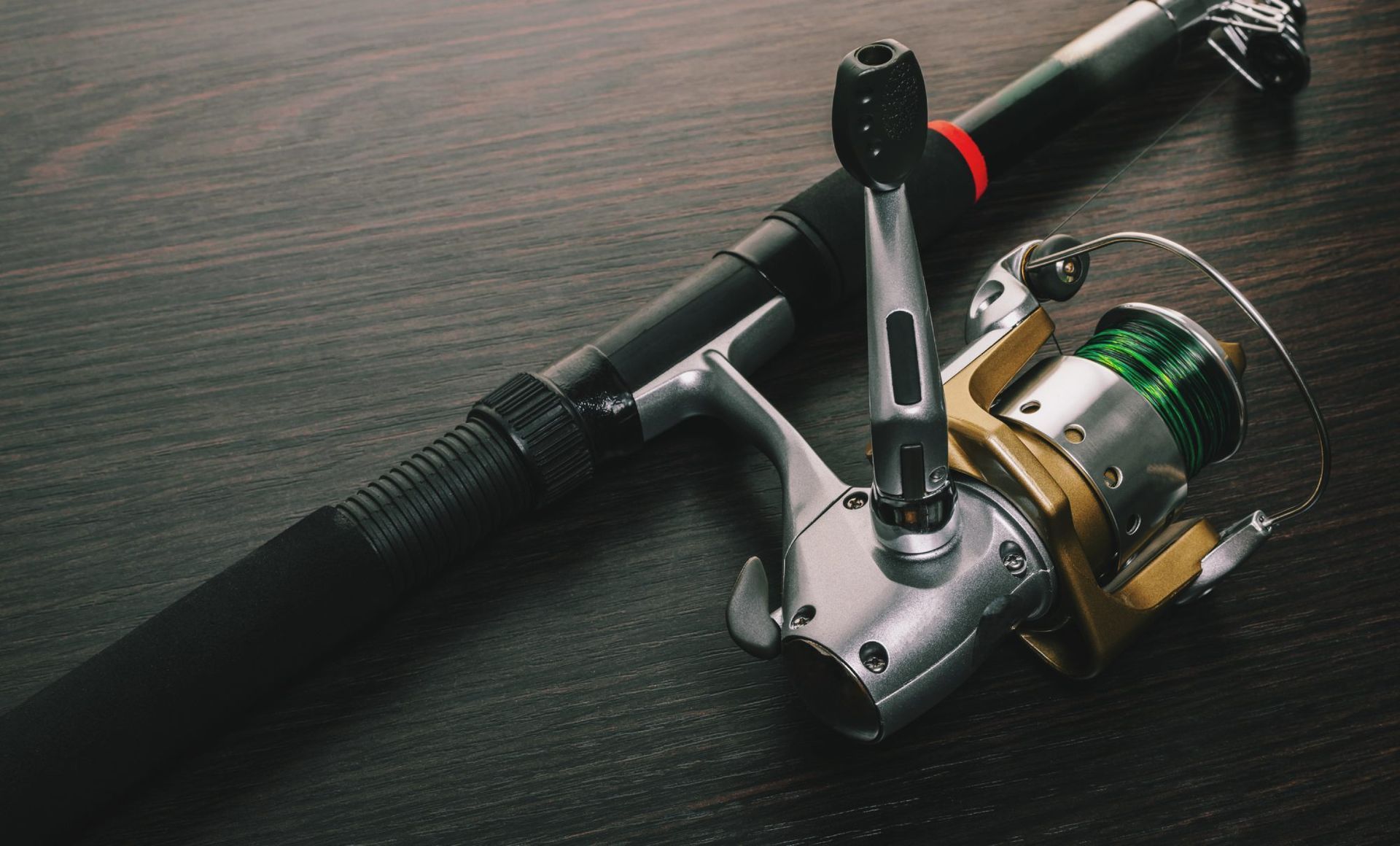 A fishing rod and reel are sitting on a wooden table.