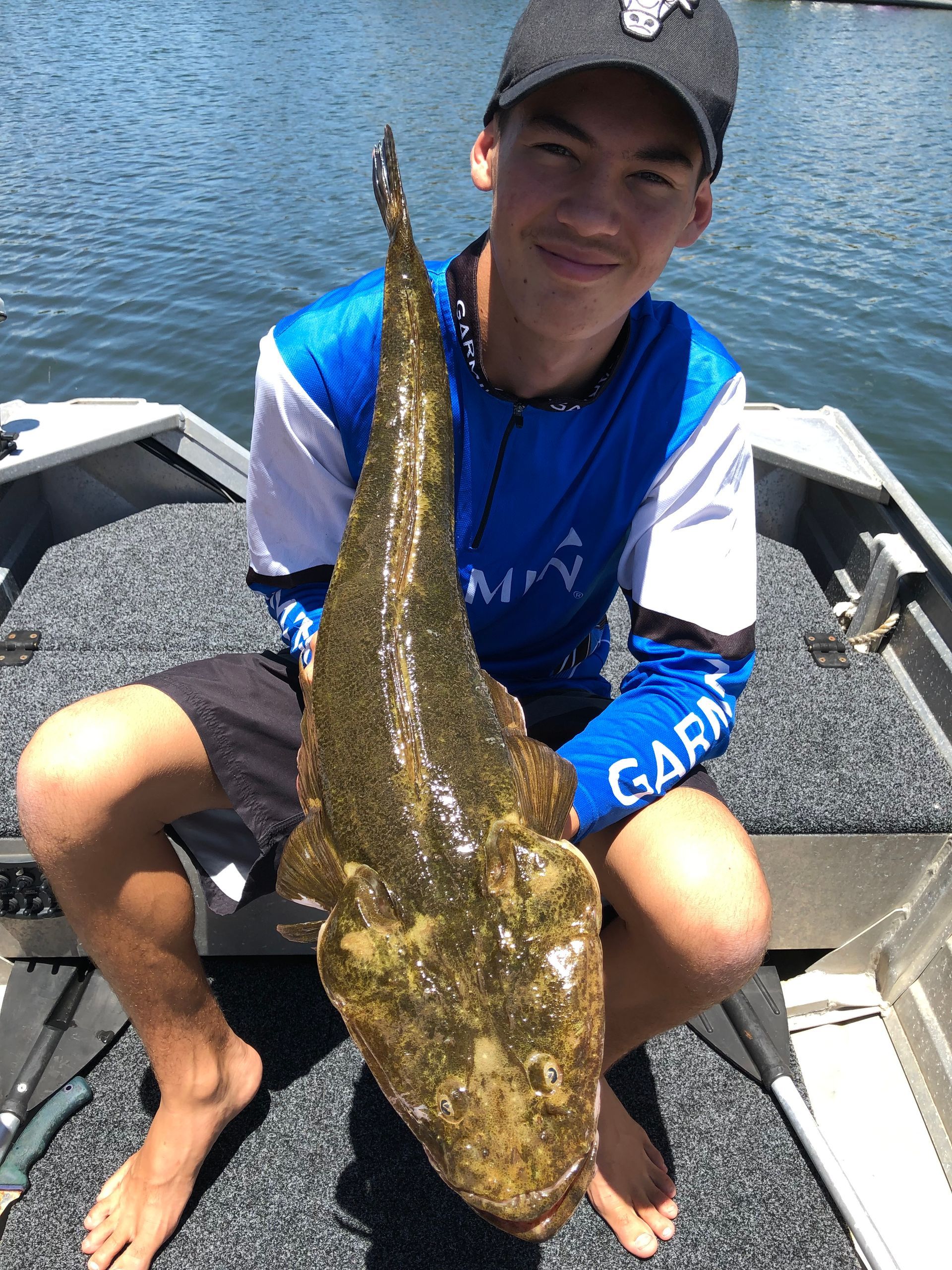 A young man is kneeling on a boat holding a large fish.