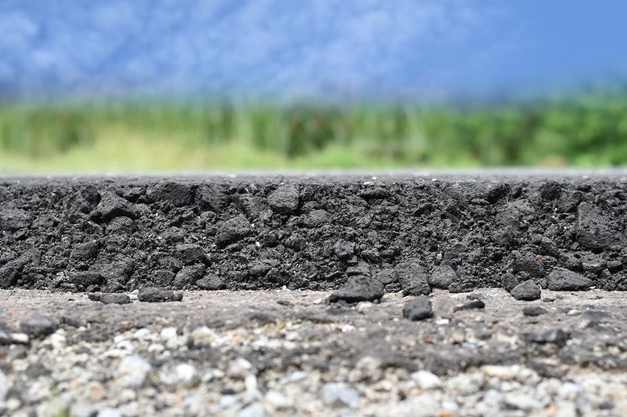 A close-up side view of a layered road showing a thick layer of coarse black asphalt over a lighter gravel sub-base.
