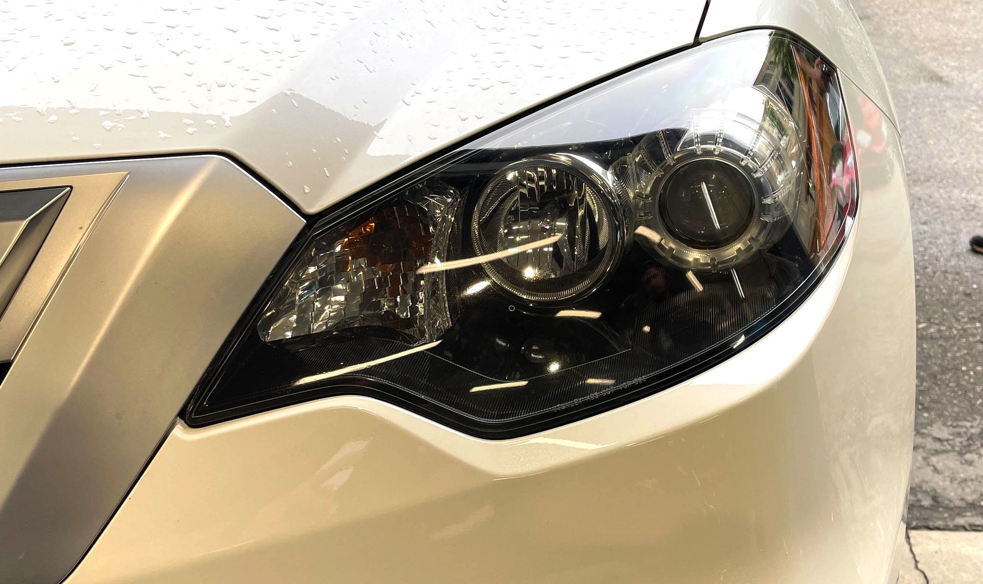 Close-up of a white car’s front headlight with a black housing and chrome trim