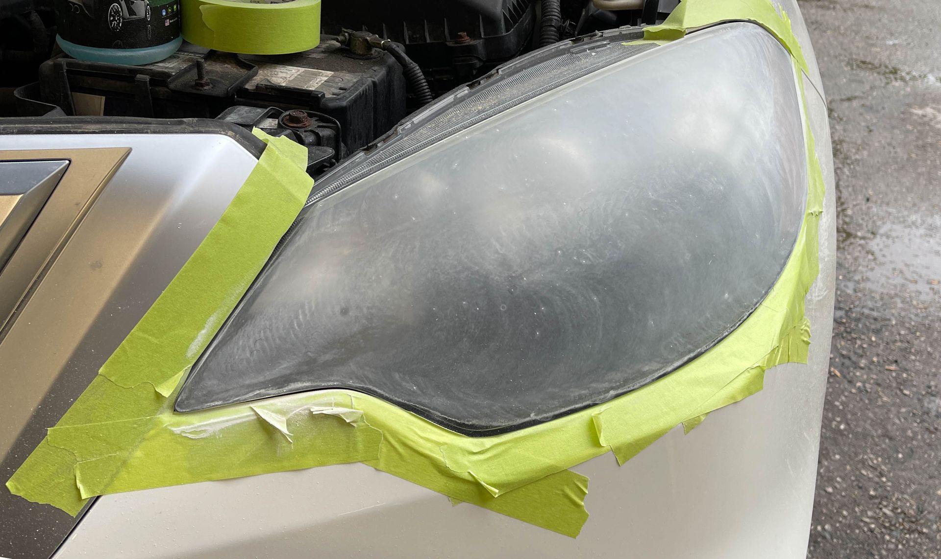 Car with hood open and taped-over headlight being repaired in a parking lot