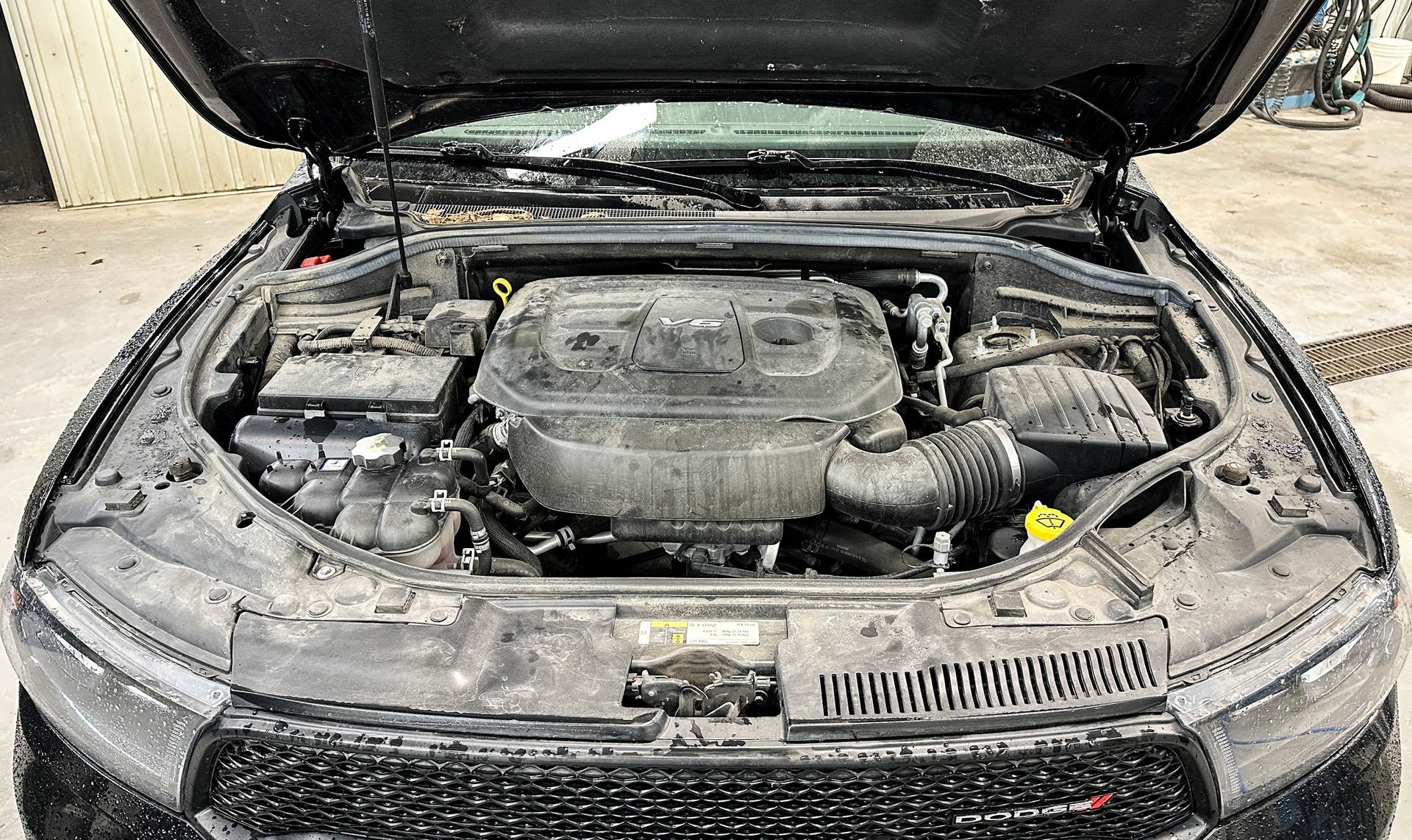 Car with hood open, showing a dusty engine compartment and front grille.